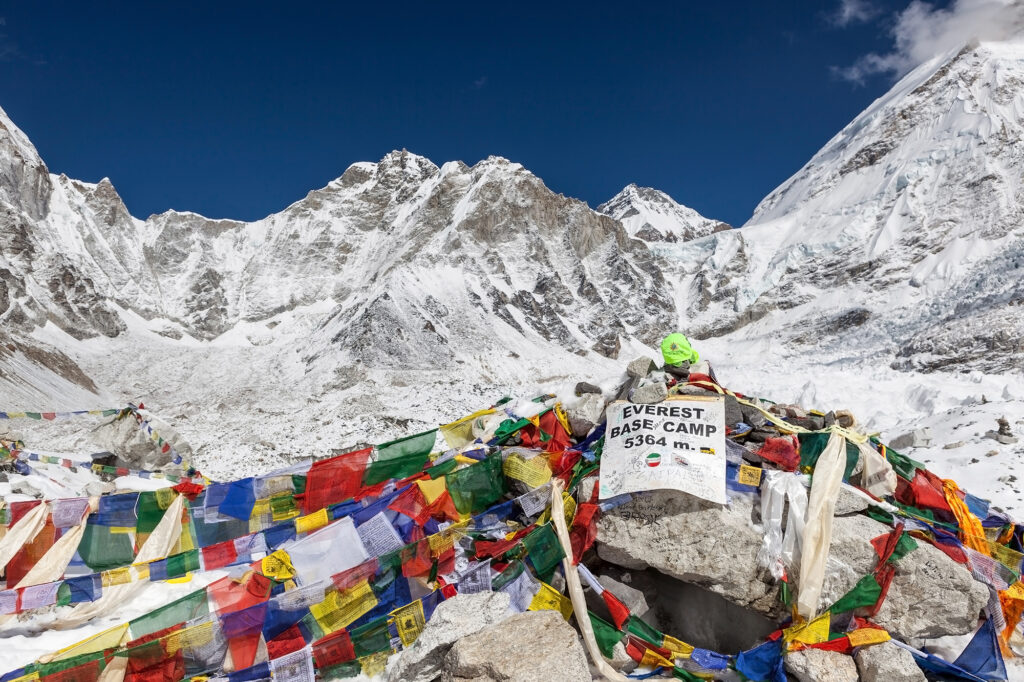 Everest Base Camp sign with stones and buddhist prayer flags and mountain Everest on the background. Everest Base Camp landmark.